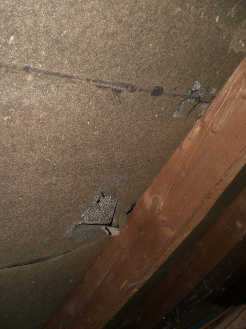 Dachbodenansicht mit dunkler Dämmung, sichtbaren Rissen und diagonalem Holzbalken im Vordergrund.