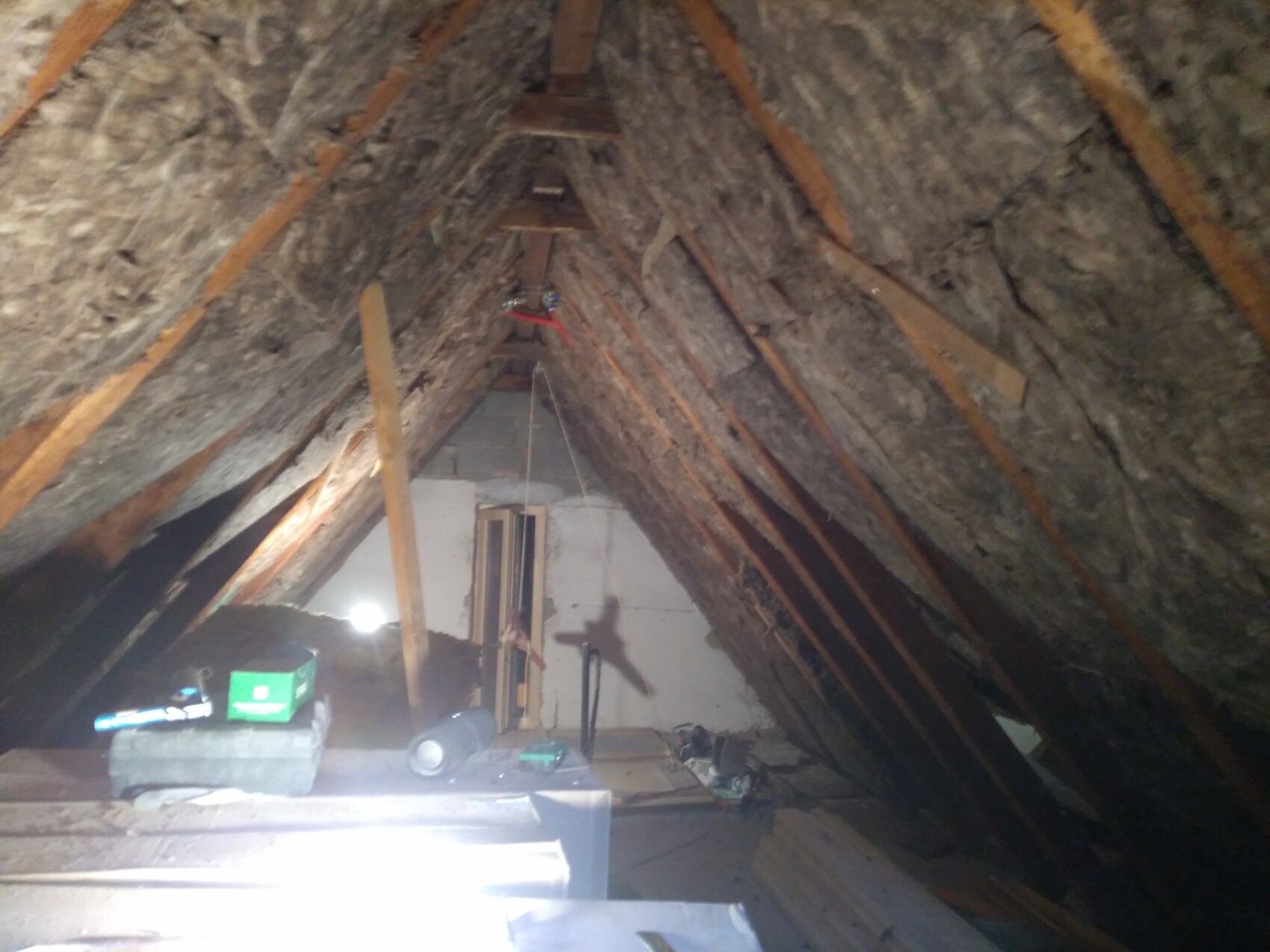 Spitzdachboden mit sichtbaren Holzbalken, Dämmung und verstreuten Werkzeugen.