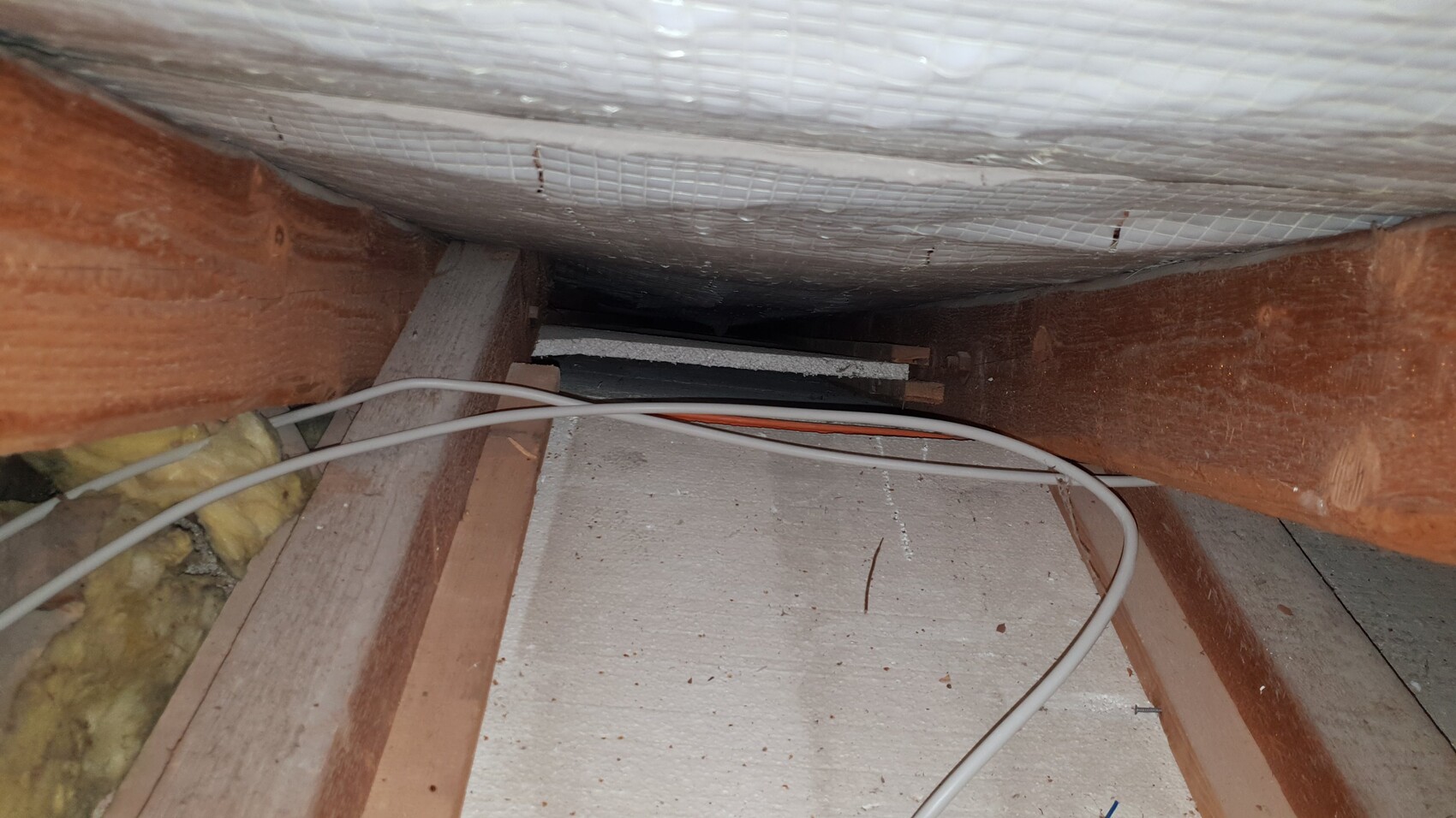 Dachboden mit Holzbalken, Dämmung und sichtbaren Kabeln