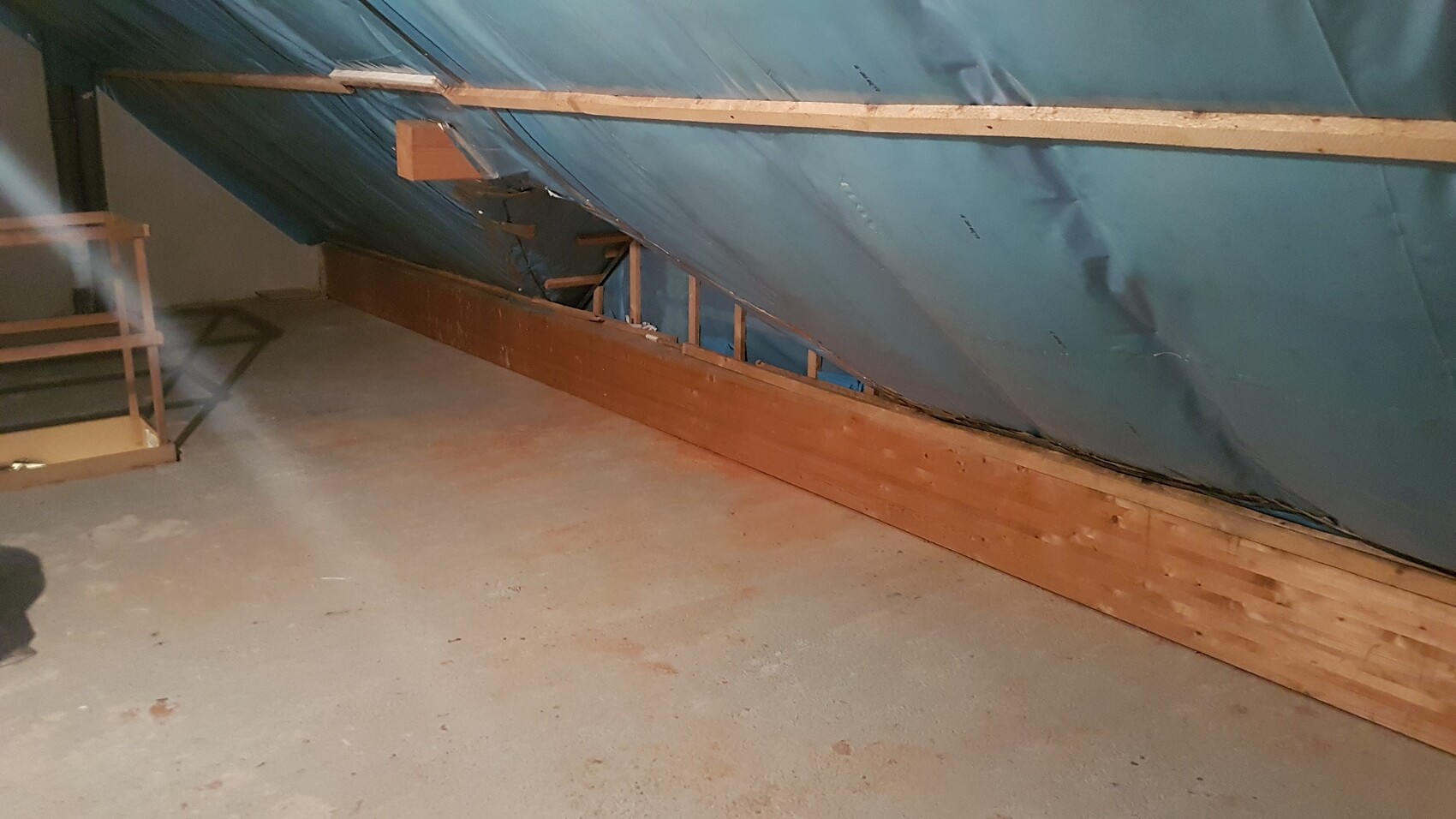 Dachboden-Rohbau mit blauer Dämmfolie, Holzbalken und provisorischem Geländer.