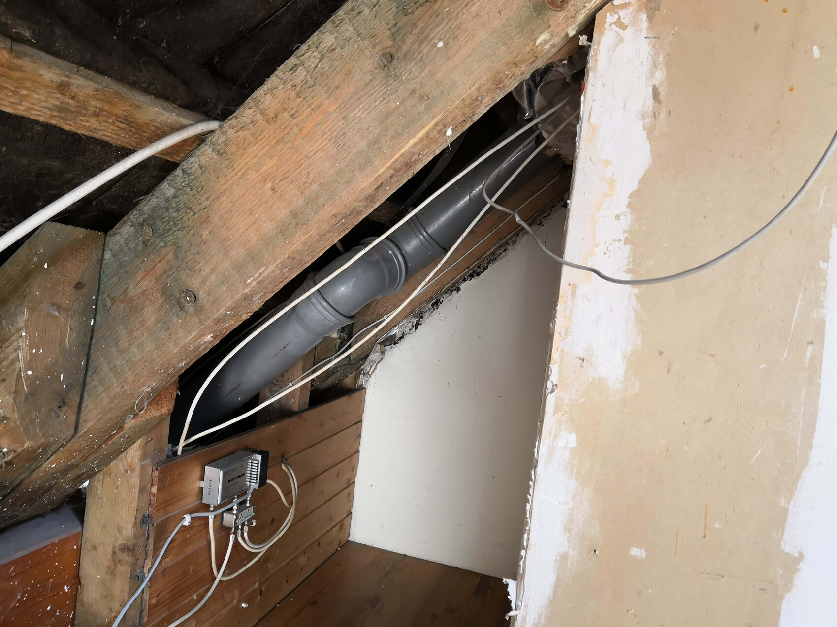 Dachboden mit Holzbalken, grauem PVC-Rohr, Kabeln und einer Elektro-Verteilerbox.