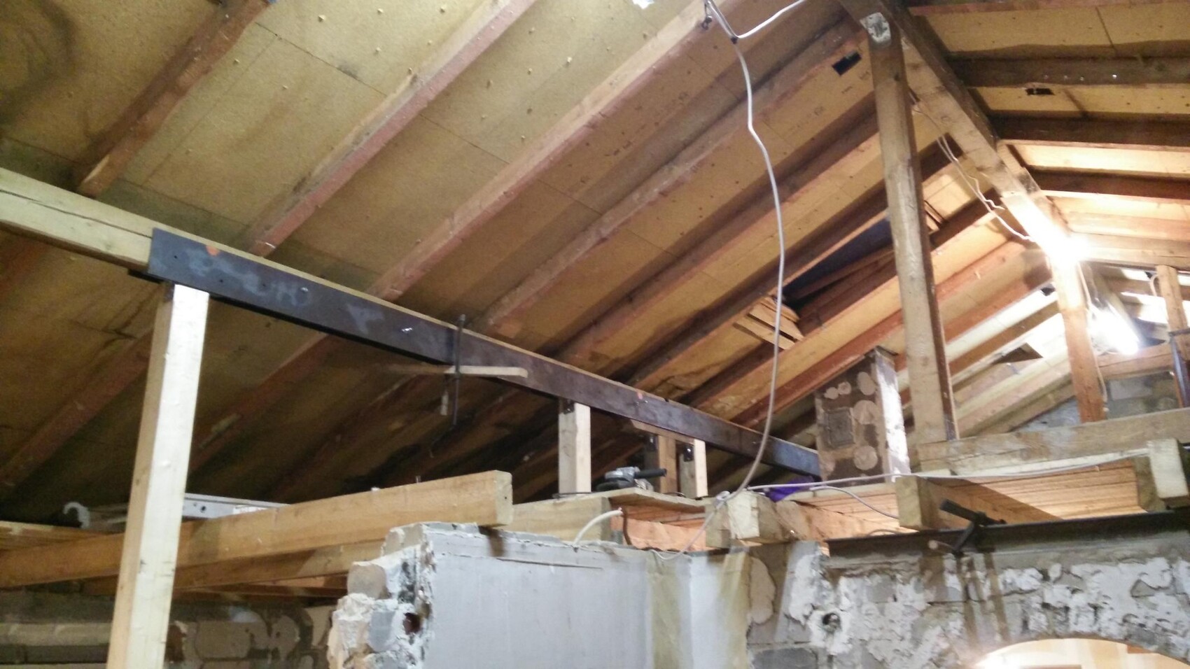 Dachboden mit Holzbalken, Kabeln und provisorischen Stützen, unzureichender Innenausbau.