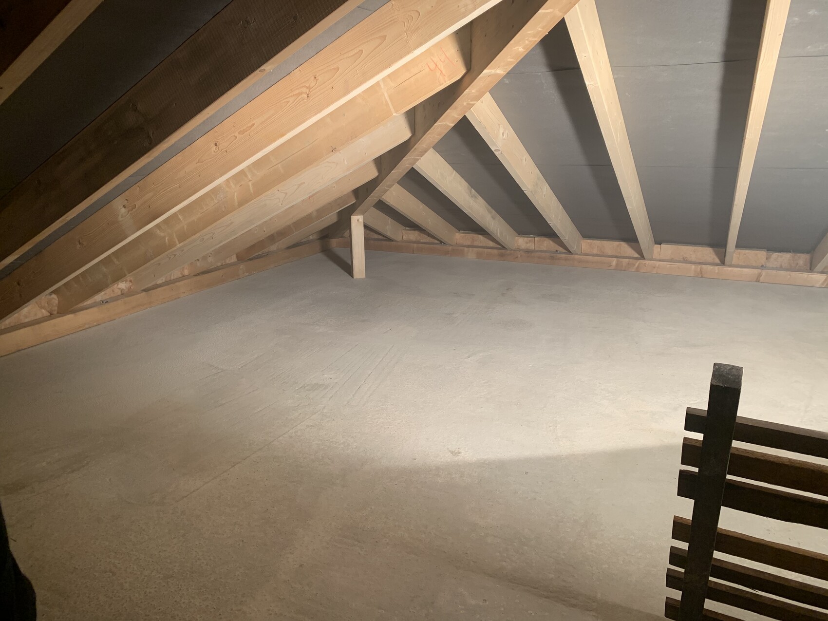 Dachboden mit sichtbaren Holzbalken, schrägen Dachstreben und einem Geländer am rechten Rand.