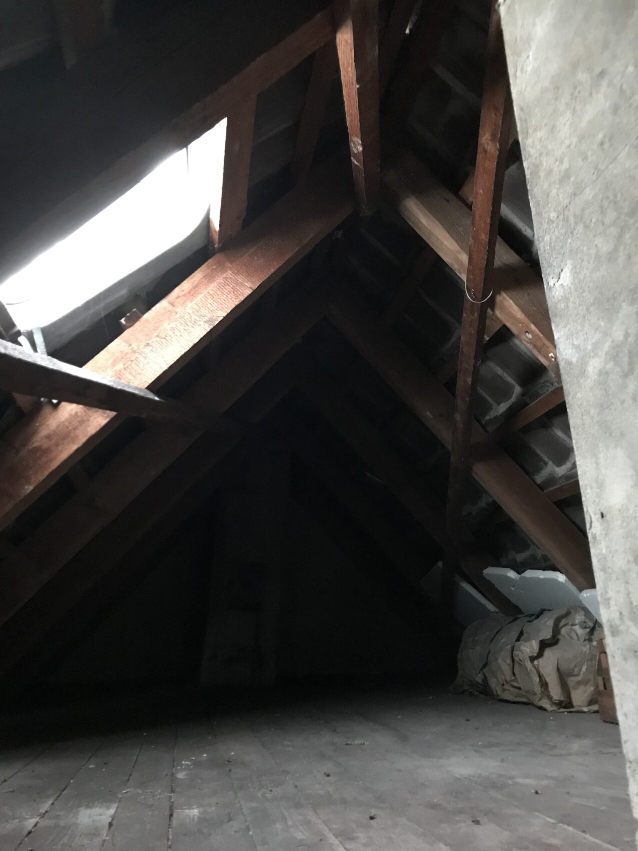 Dachboden mit Holzbalken und Sparren im Dachgeschoss, dunkler Boden.