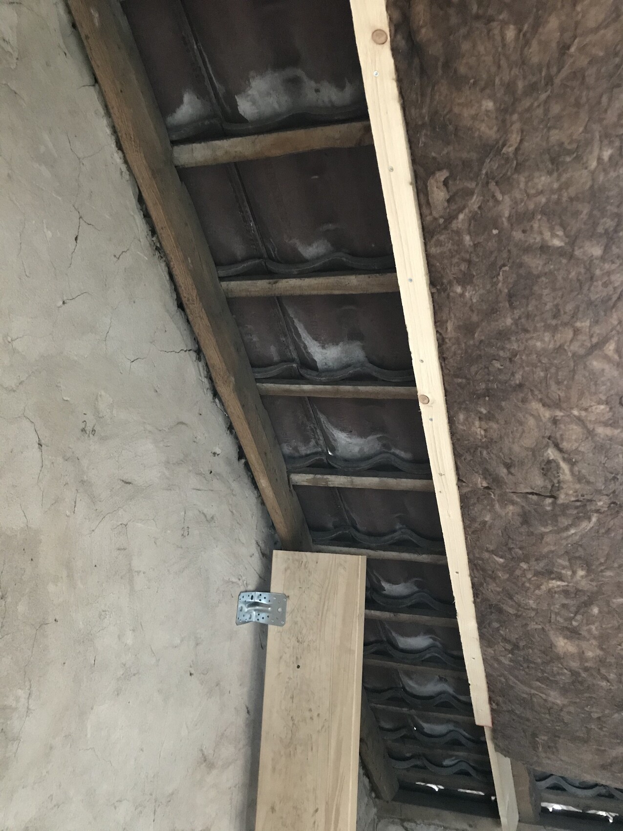 Dachbodenansicht: Holzbalken, Dachziegel, Dämmung und eine provisorische Holzkonstruktion.