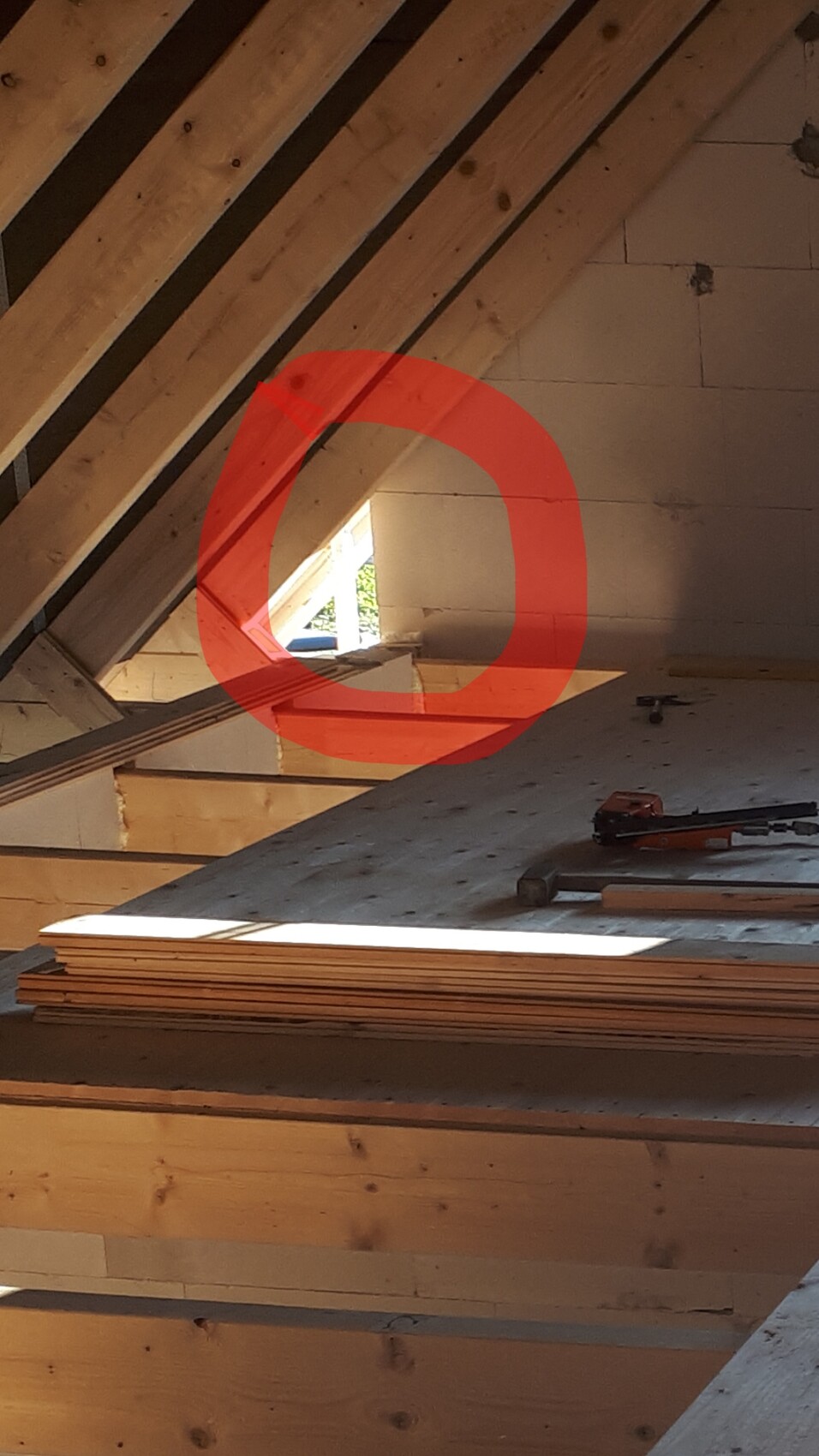 Bauarbeiten im Dachstuhl: sichtbare Holzbalken, Holzplatten und Werkzeuge, roter Kreis markiert.