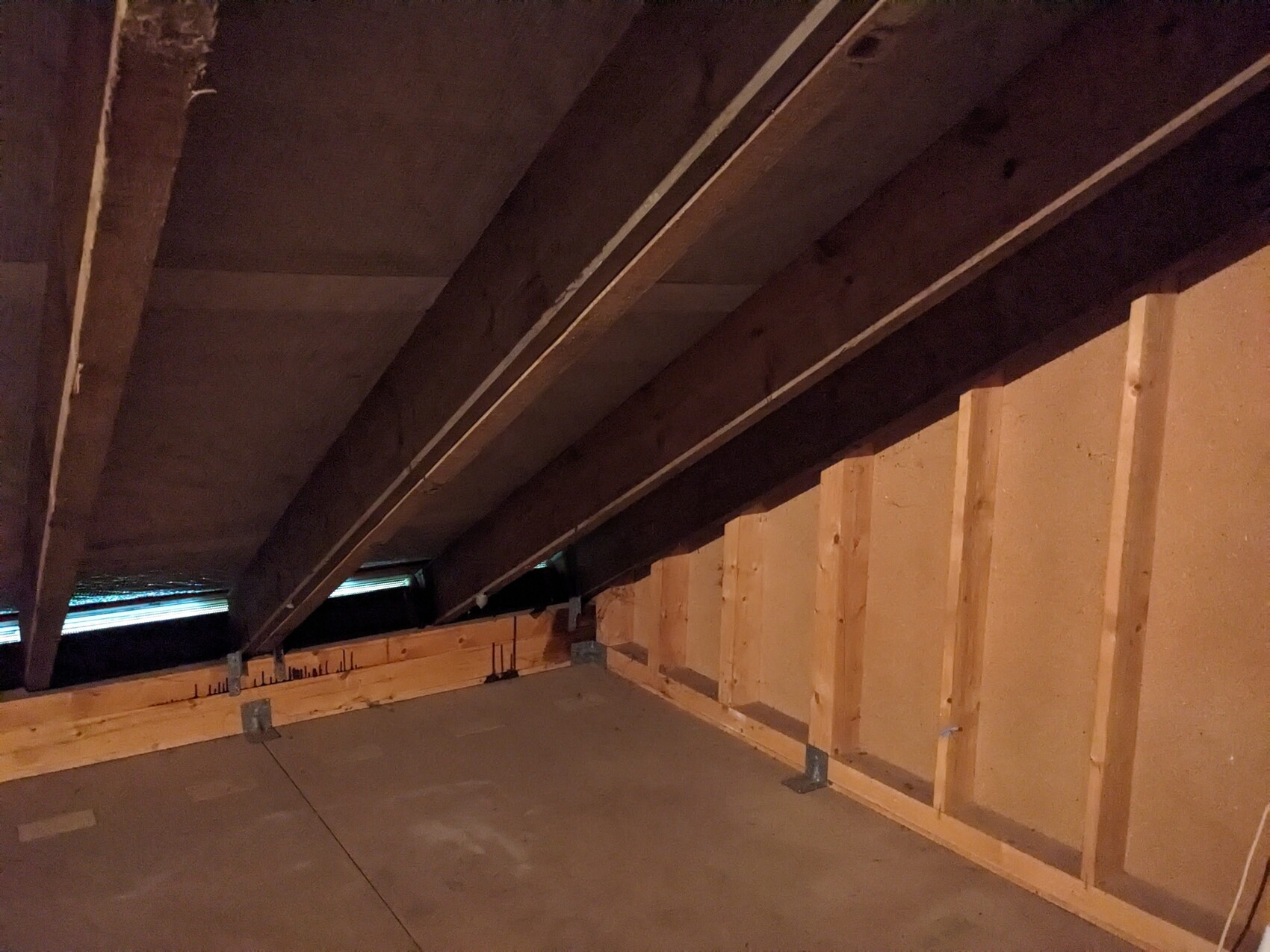 Dachboden: Holzbalken, Ständerwerk und Betonboden, geringe Beleuchtung.