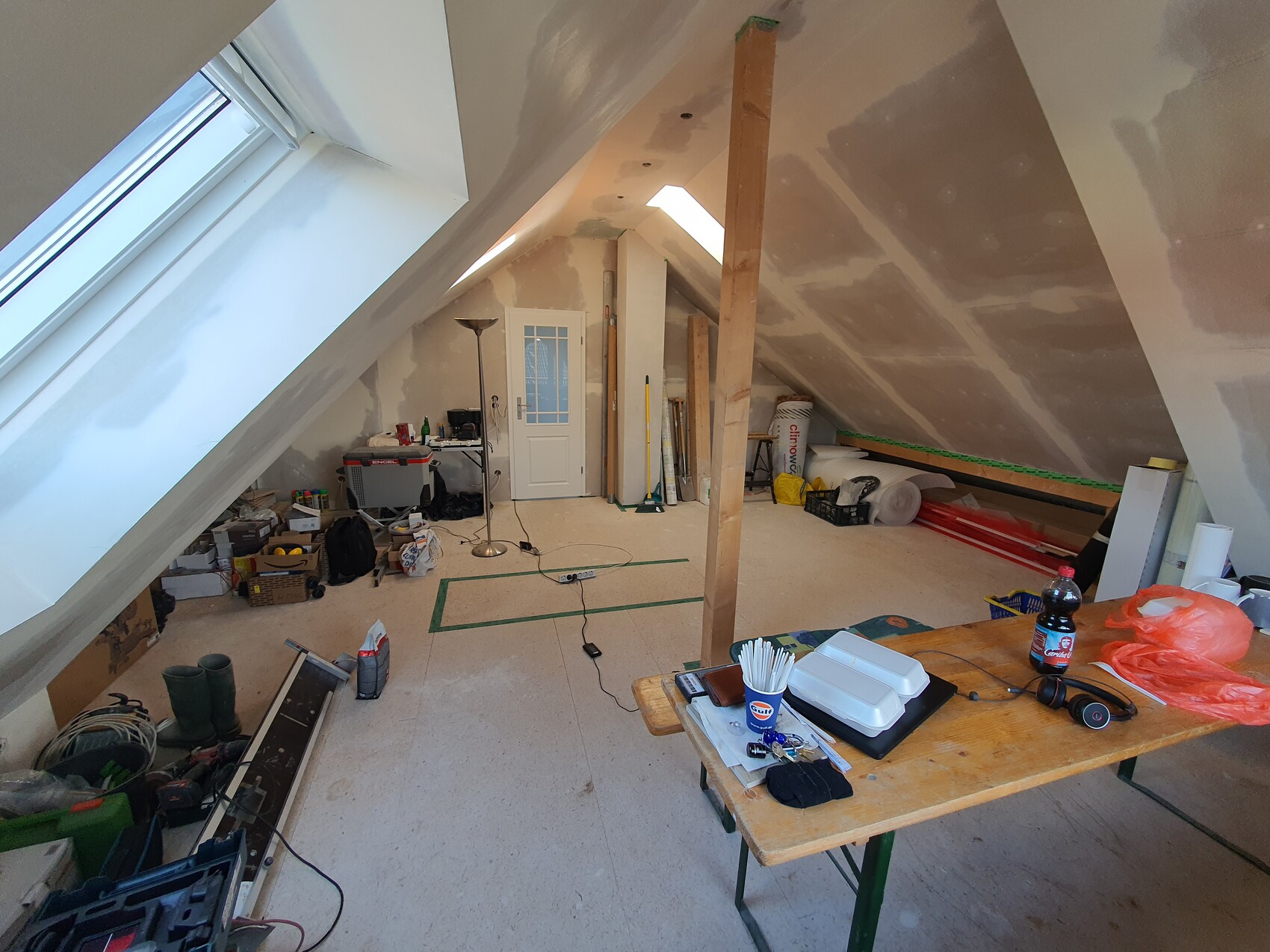 Dachbodenwerkstatt: schräges Dach, Dachfenster, Tür hinten, Tisch mit Boxen und Werkzeug.
