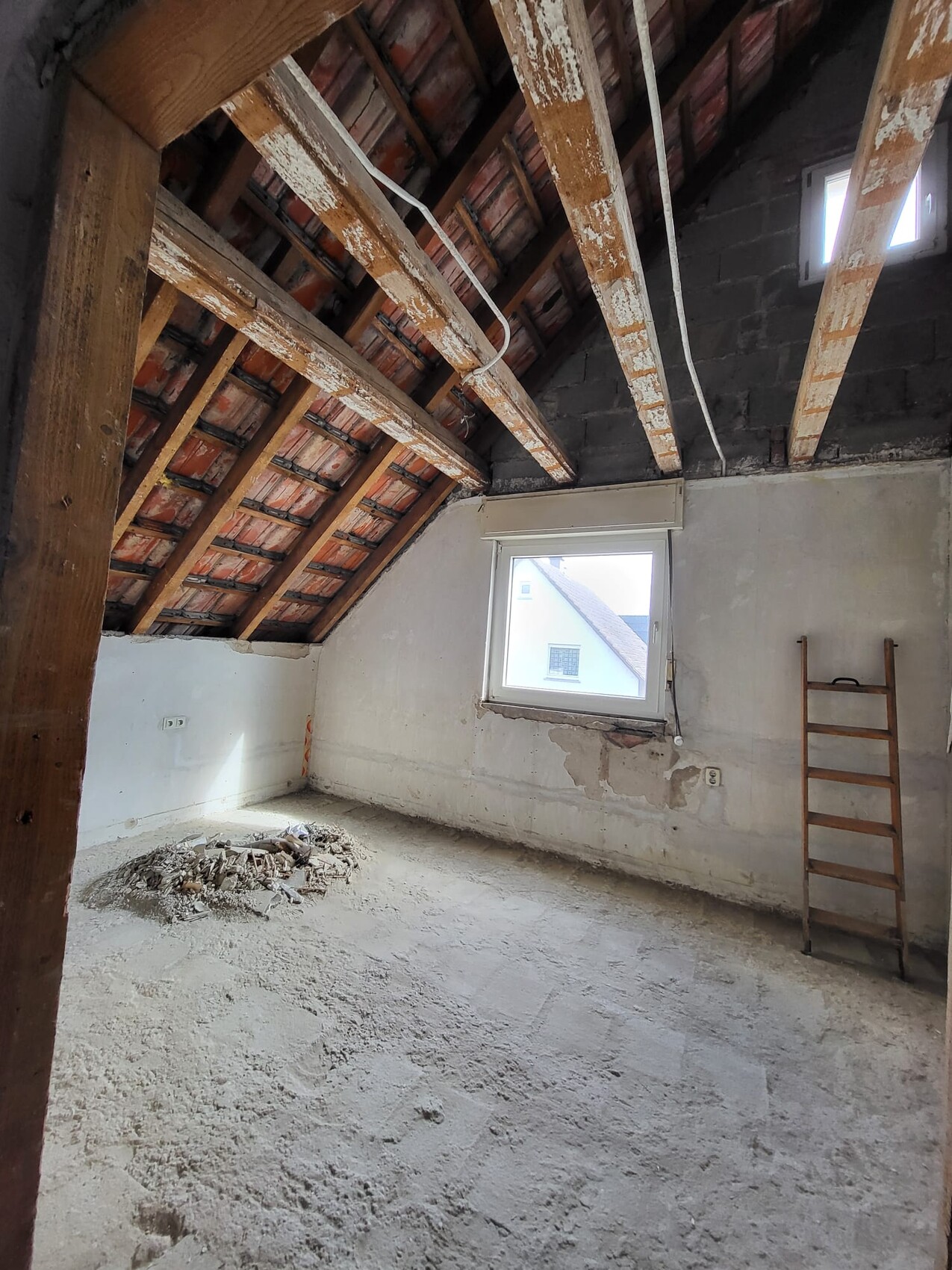 Unrenovierter Dachboden mit Holzbalken, Fenster, Leiter und Bauschutt.