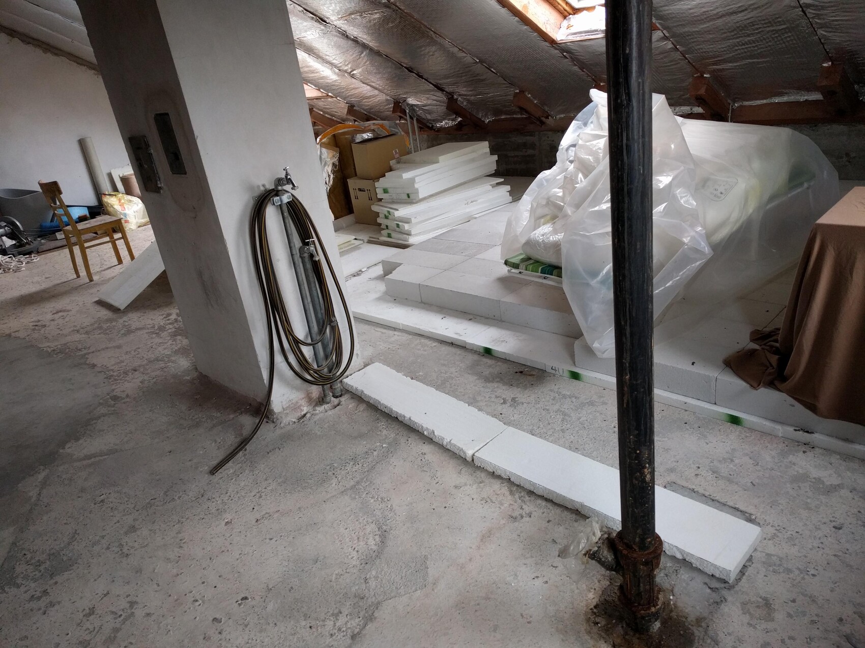 Dachbodenrenovierung: Styroporplatten gestapelt, Schlauch an Säule, Plastiktüte über Gegenstand.