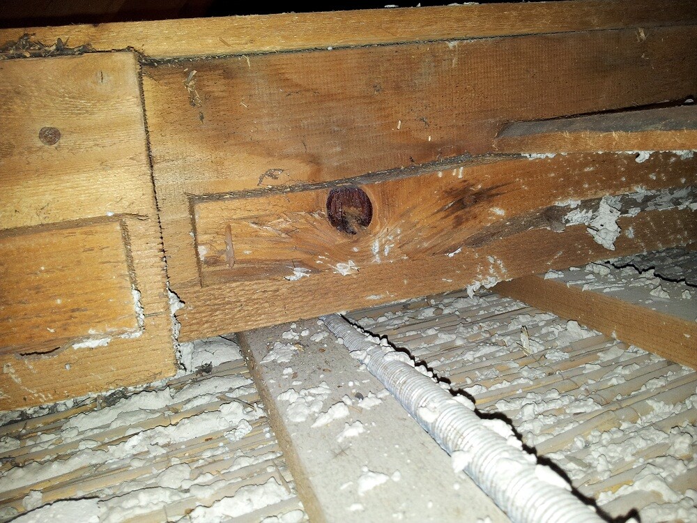 Dachboden-Rohbau mit Holzbalken, sichtbarer Isolierung und Kabelrohr im Staub