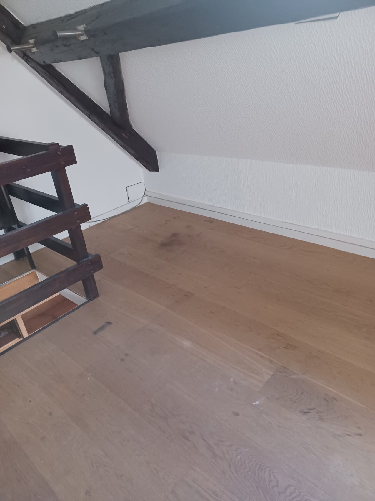 Dachboden mit dunklen Holzbalken, weißer Wand, Holzboden und Treppengeländer an der Seite