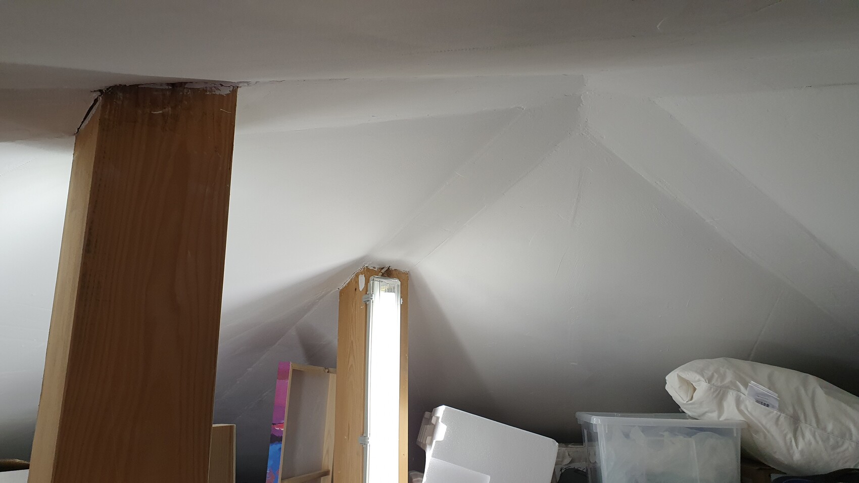 Dachboden mit schräger Decke, Holzstütze und einer vertikalen Leuchtlampe, Lagergut.