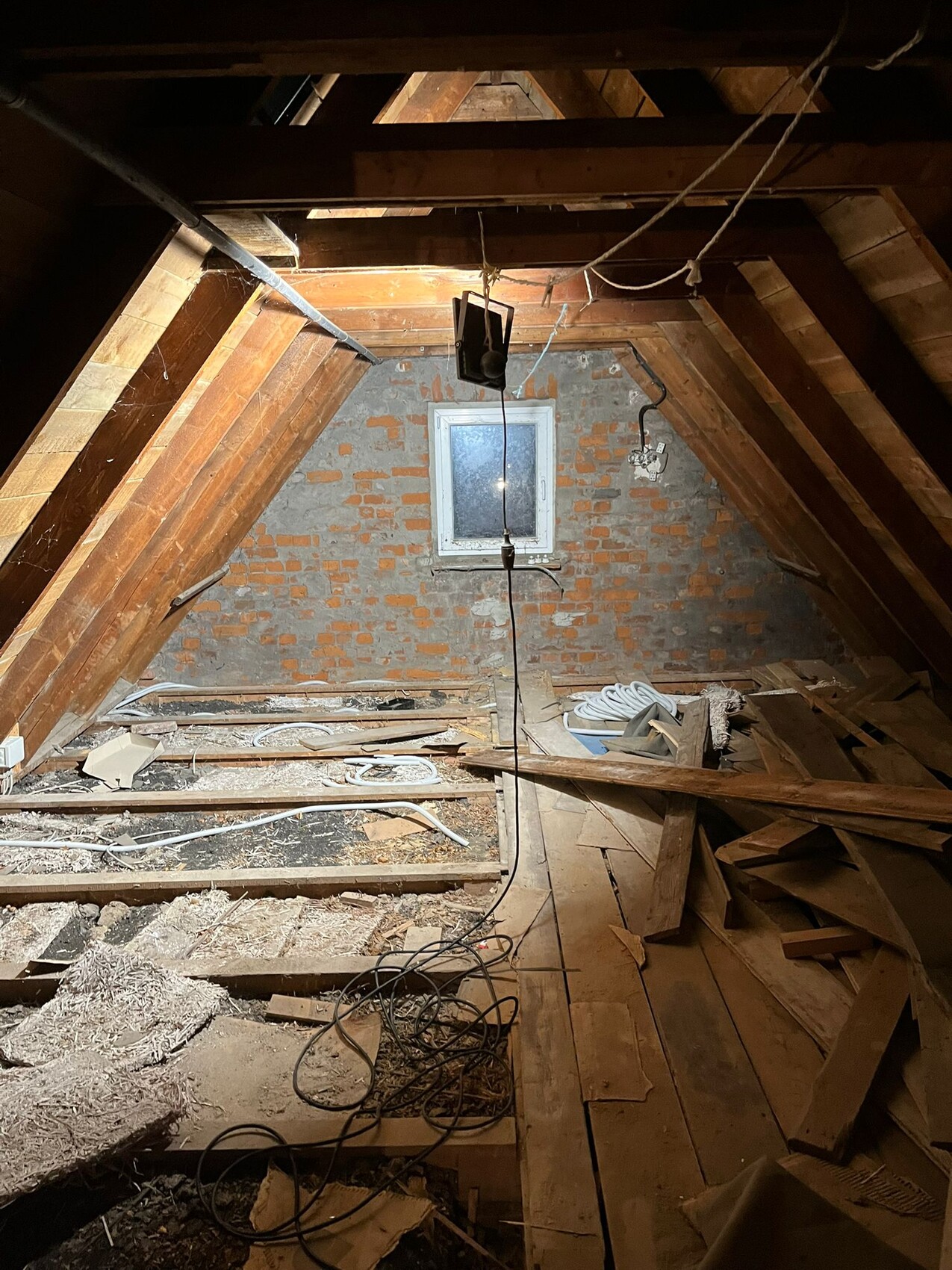 Dachboden mit Holzbalken, bröckelnde Backsteinwand, Kabel, Holzreste und Staub.