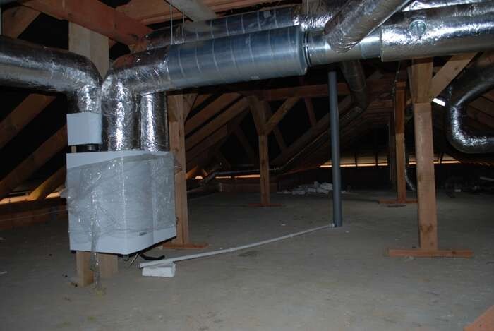 Dachboden mit silbernen isolierten Lüftungsrohren, Holzbalken und Heizungsanlage.