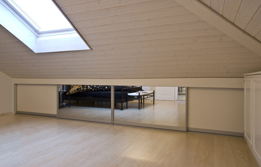 Dachgeschossraum mit schräger Holzdecke, Dachfenster und Spiegelschiebetüren; Bett sichtbar.