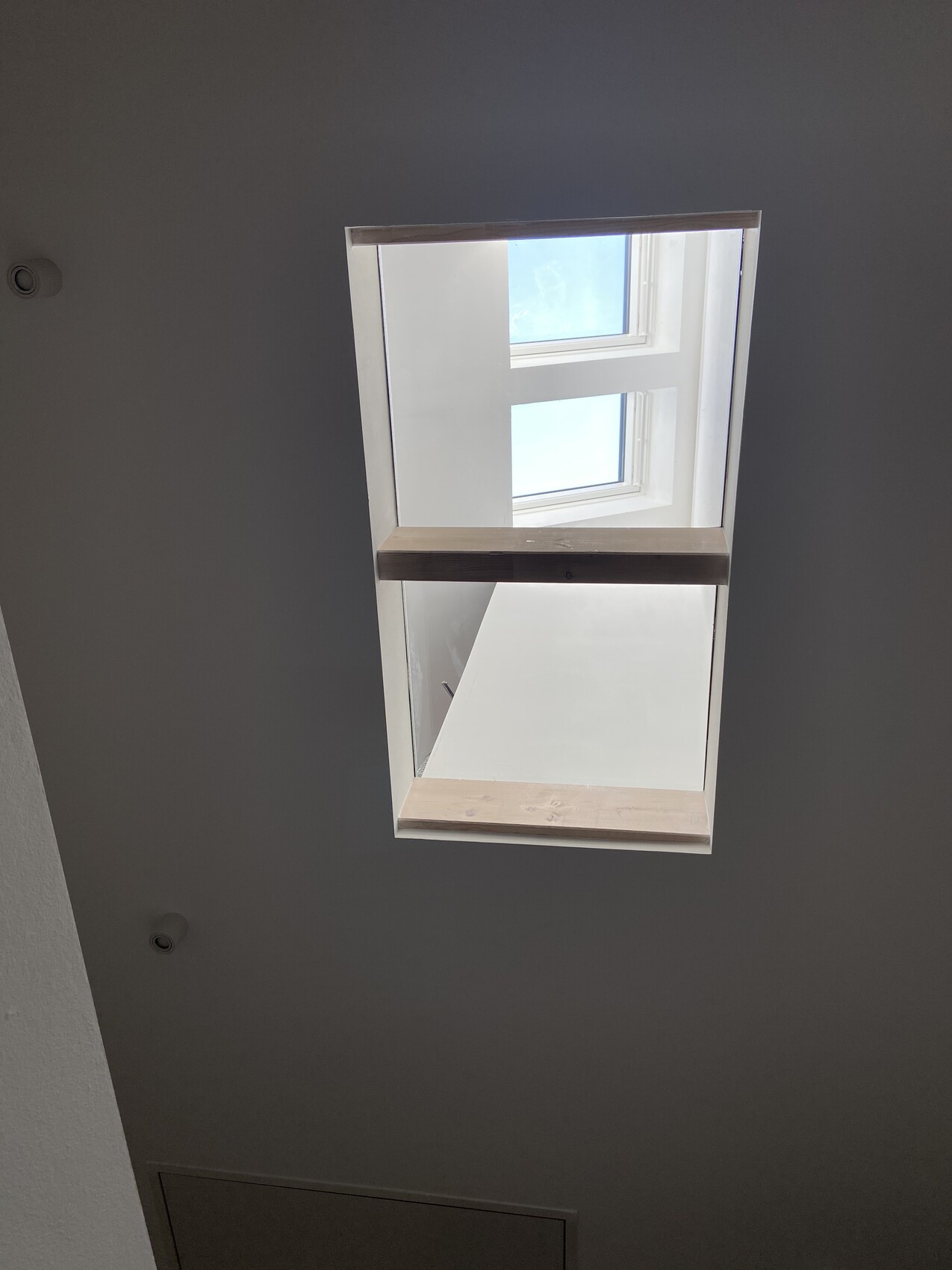 Helles Dachfenster (Skylight) in weißer Decke mit Holzrahmen, Blick nach draußen.