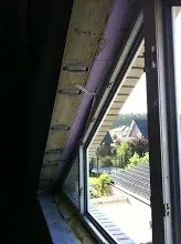 Innenaufnahme eines Dachraums mit offenem Dachfenster, Balkenrahmen und Baumaterialien