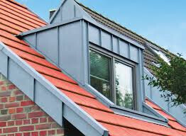 Dachgaube mit Fenster über rotem Ziegeldach eines Hauses unter blauem Himmel.