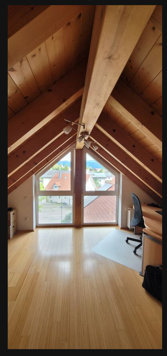 Helles Dachgeschossarbeitszimmer mit Holzbalken, großer Fensterfront und Schreibtischstuhl