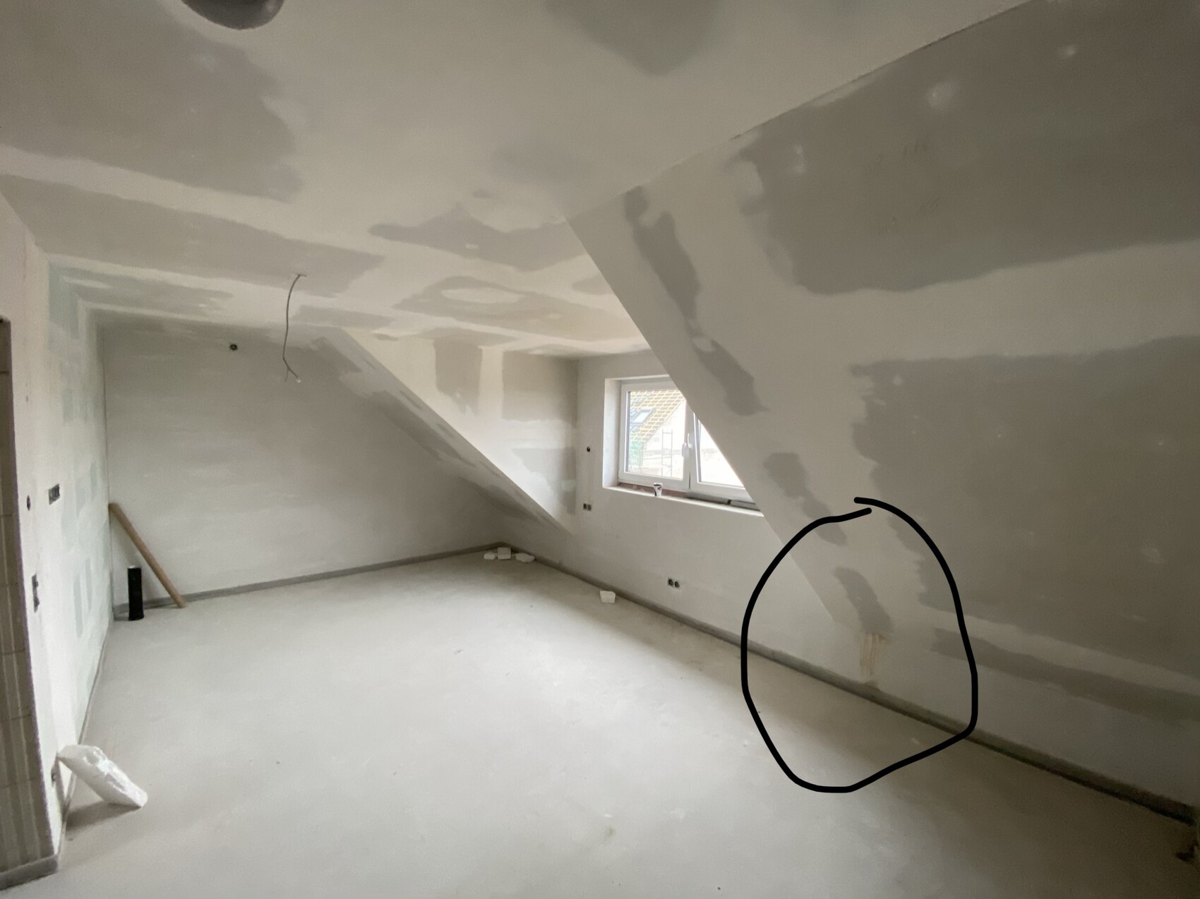 Unrenovierter Dachgeschossraum mit schräger Decke, Fenster und ungleichmäßigen Putzflächen.