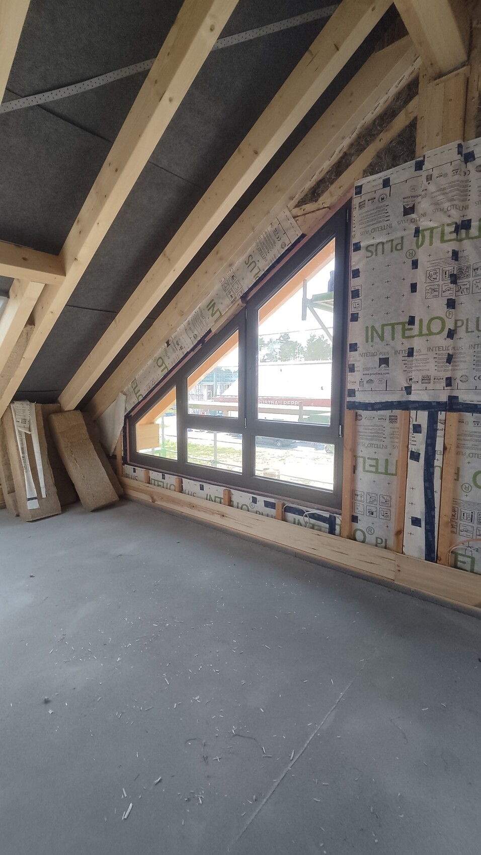 Dachgeschoss-Rohbau mit Holzrahmen, schrägem Fenster und Dämmmaterial an der Wand.