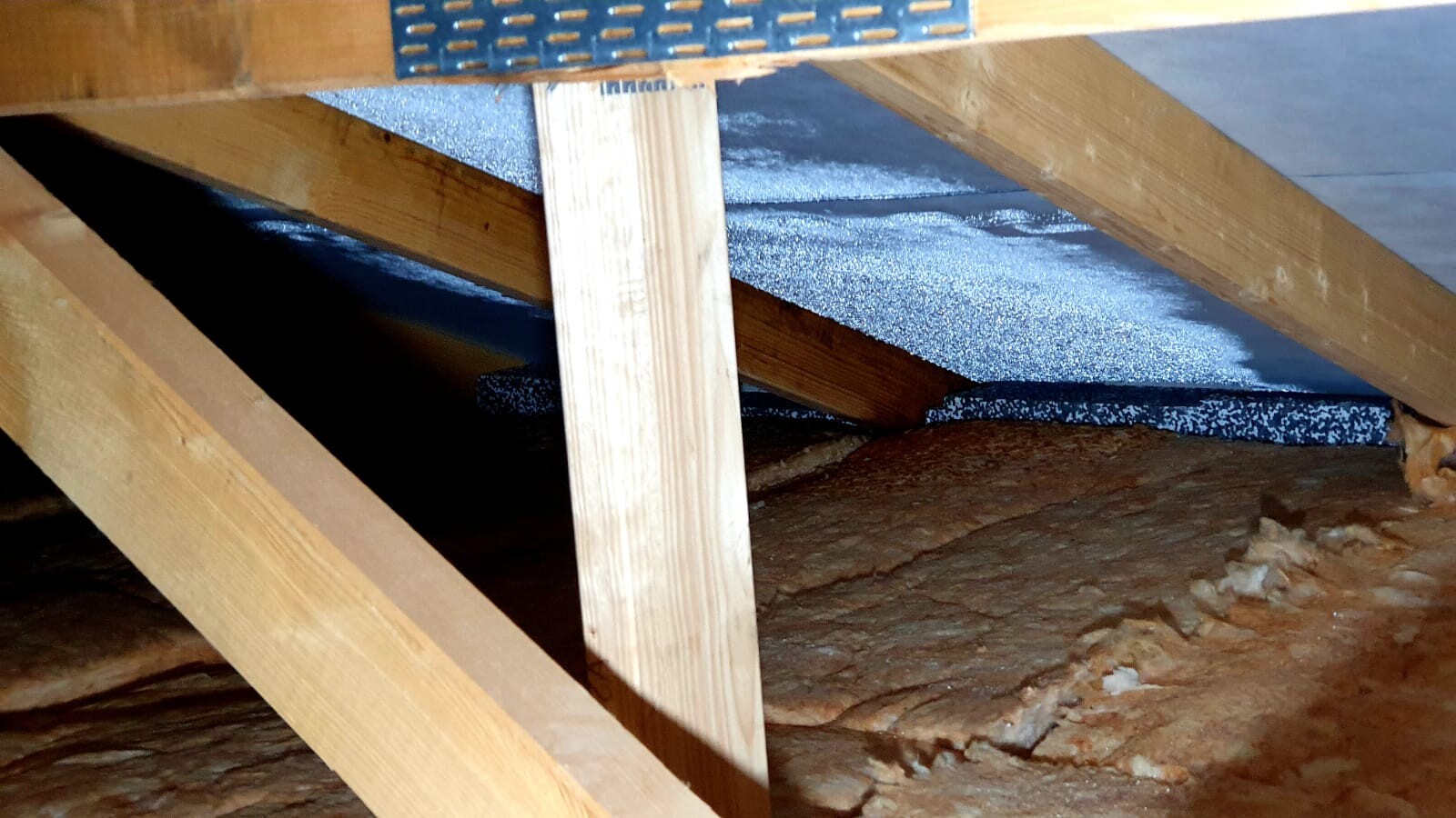 Dachboden mit Holzbalken, Dämmung und blauer Folie zwischen den Holzbalken.
