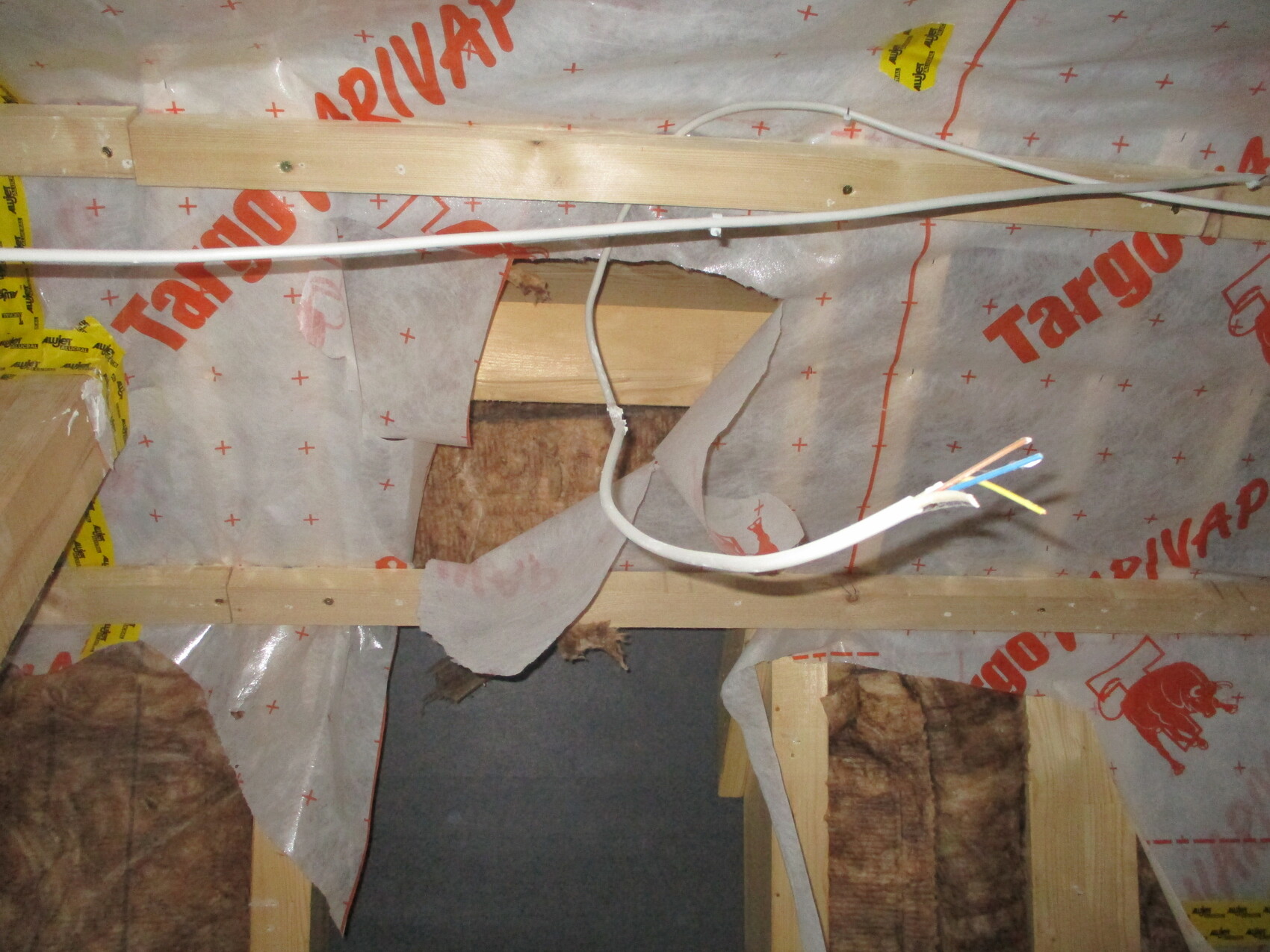 Unfertiger Innenbereich mit Holzständern, Dämmung, Folie und freiliegendem Kabel.