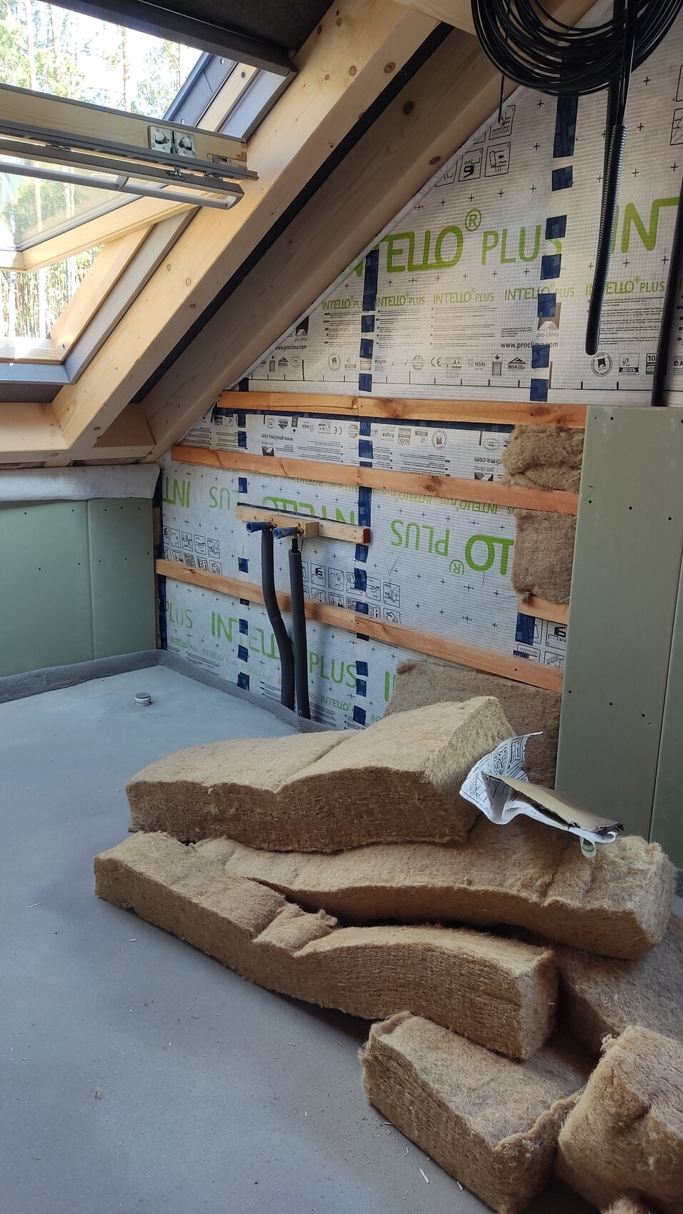 Dachboden-Innenraum mit Dachfenster, Holzlatten an der Wand und losen Dämmplatten aus Steinwolle.