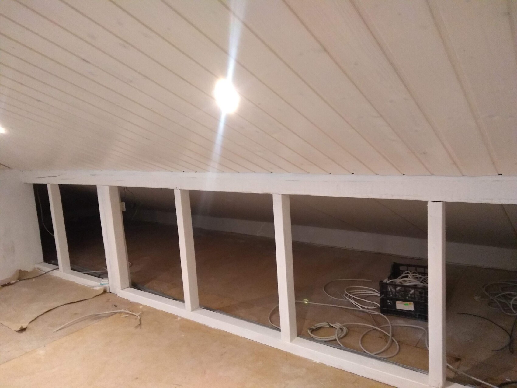 Dachgeschoss mit schräger heller weißer Decke, weißem Holzrahmen und sichtbaren Kabeln