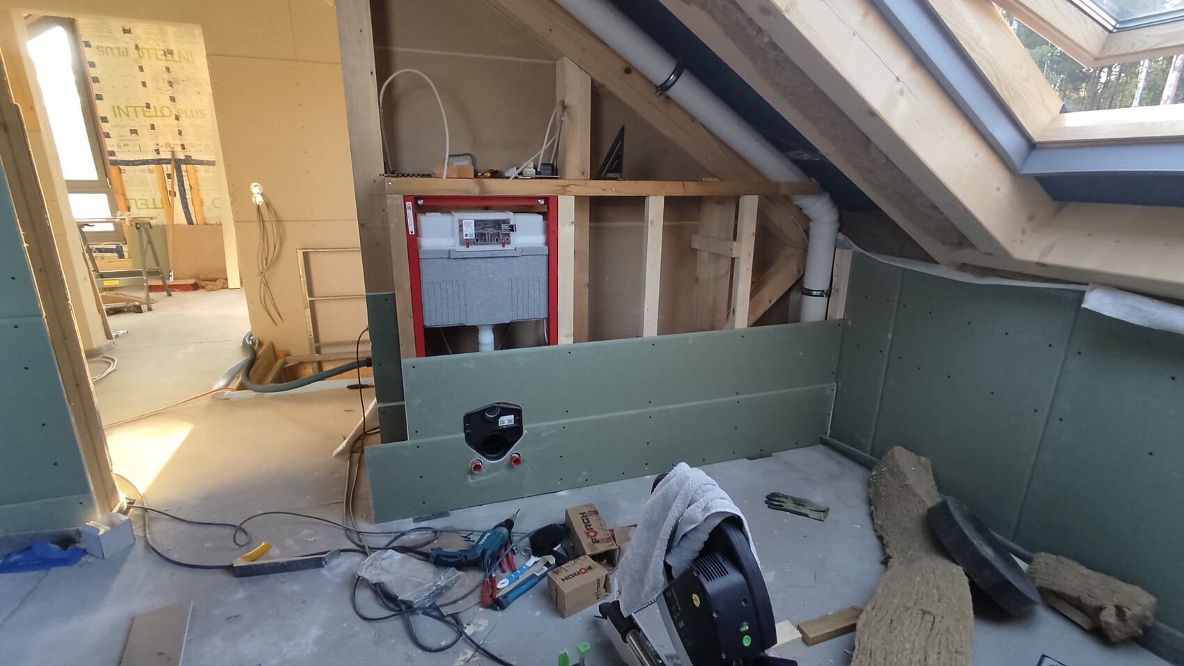 Dachgeschoss-Baustelle im Ausbau: Dachfenster, grüne Gipskartonplatten, Werkzeuge und Rohbau.