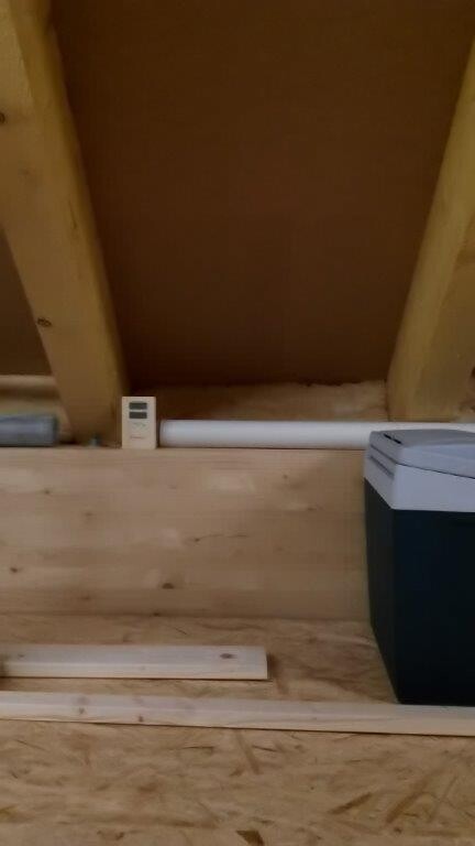 Dachboden mit sichtbaren Holzbalken, Holzplatten und einer Waschmaschine an der Seite