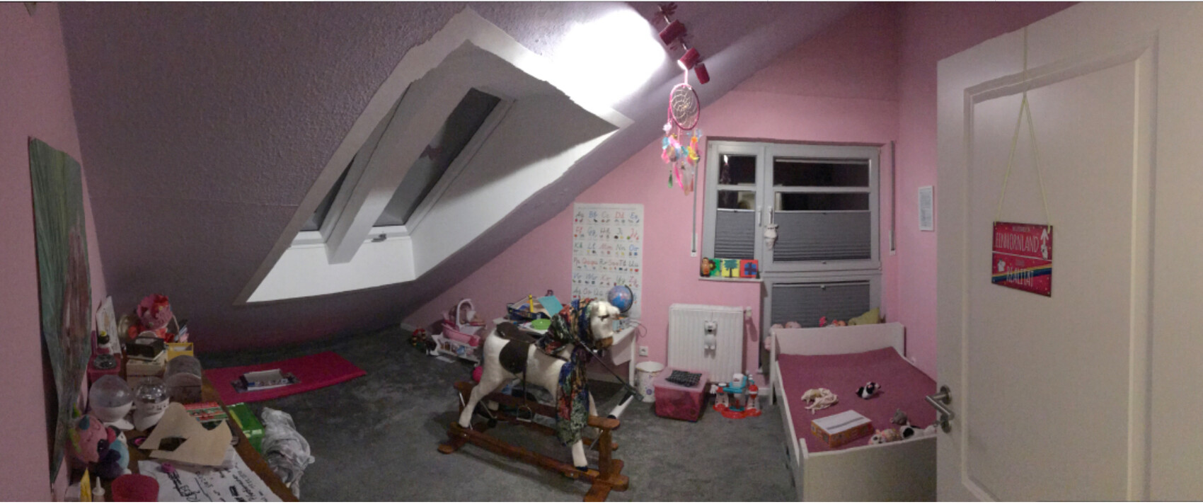 Dachboden-Kinderzimmer in Rosa mit schrägen Fenstern, Spielzeug, Schaukelpferd und Bett.