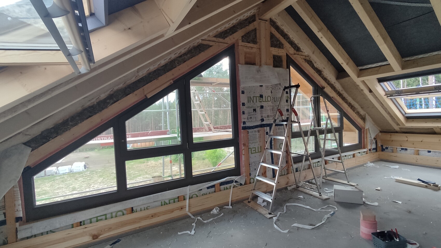 Unfertiger Dachbodenraum: Holzkonstruktion, große Dachfenster, Leiter und Baumaterialien.