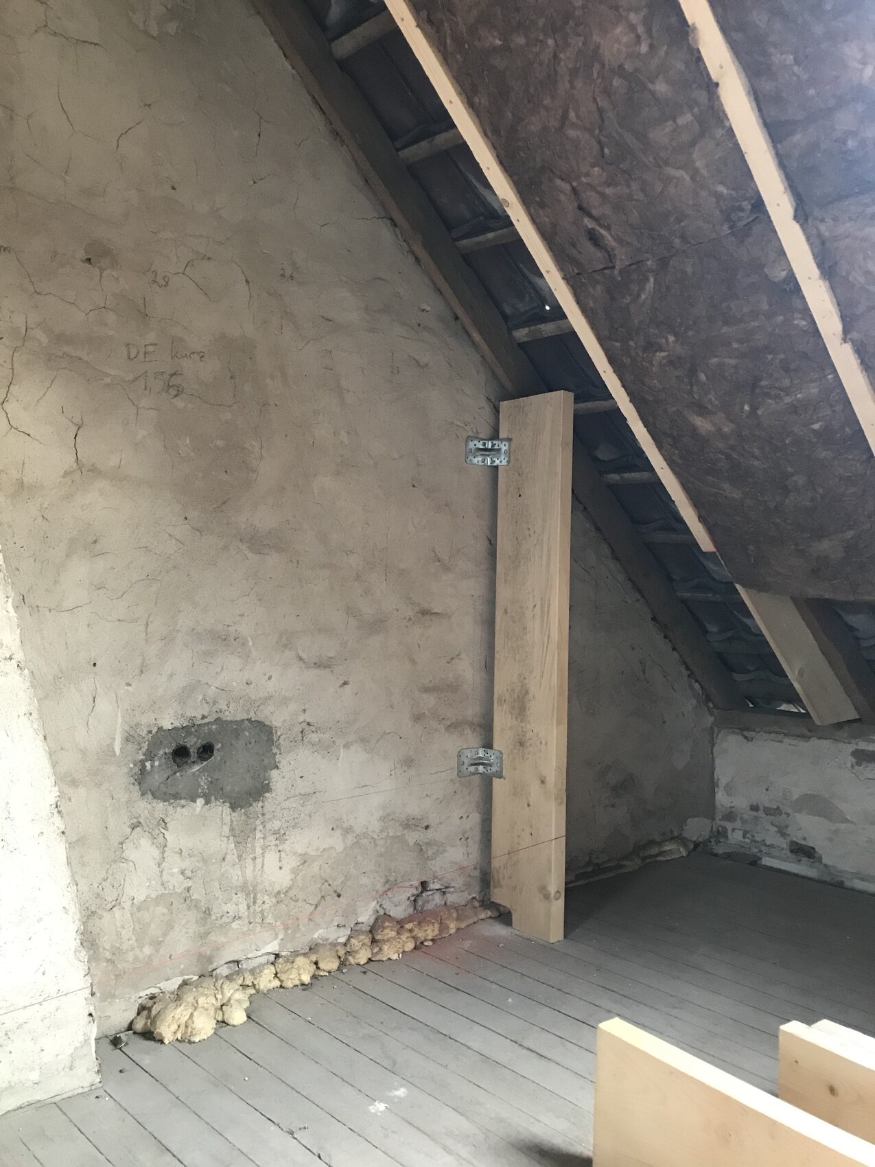 Unfertiger Dachboden mit sichtbaren Holzbalken, Rohbauwänden und Dämmung im Dachbereich.