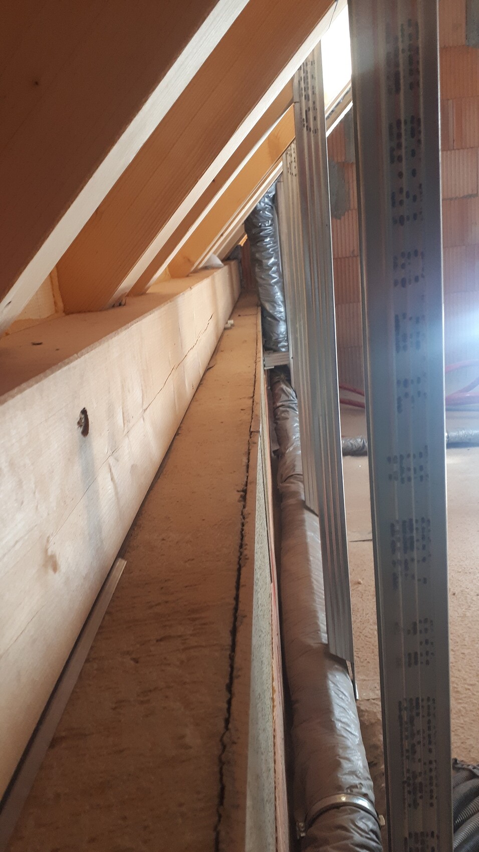 Dachbodenansicht: Holz- und Metallrahmen, Dämmung und isolierte Rohre entlang der Wand.