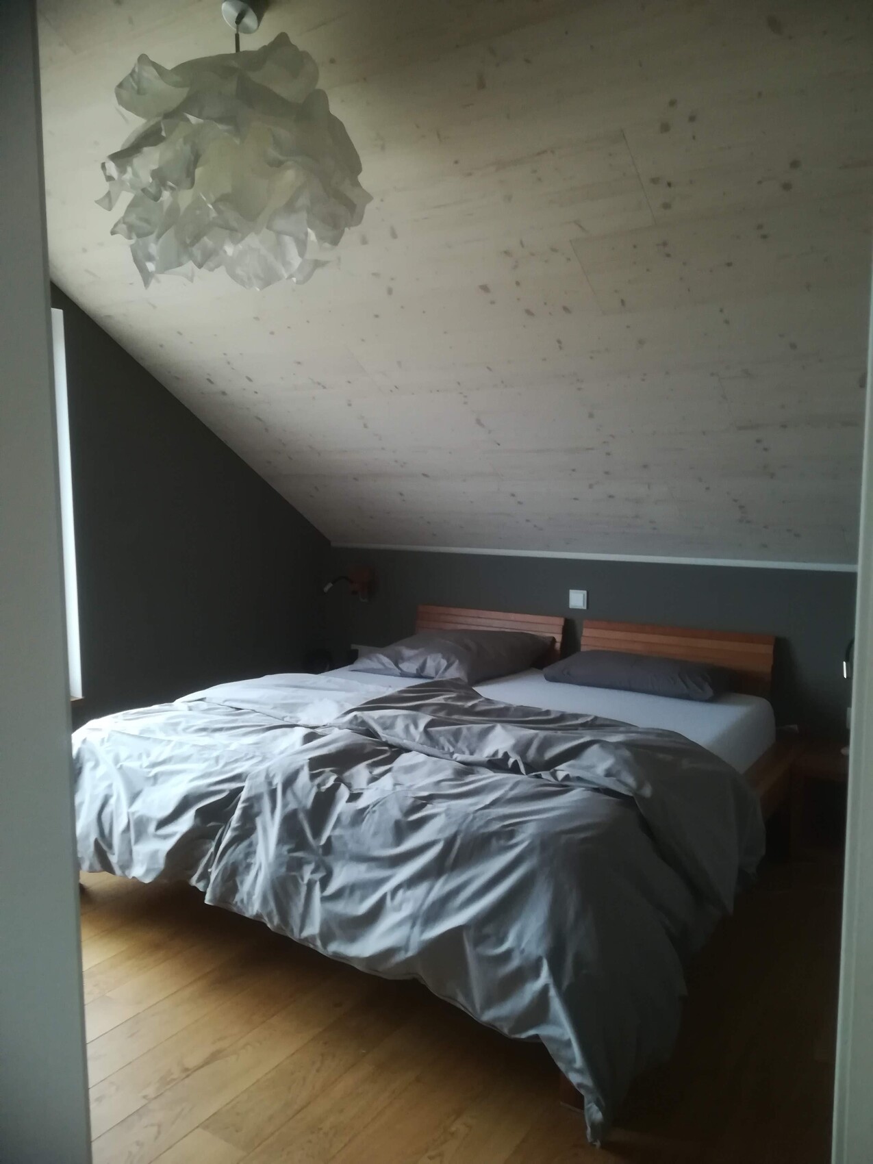 Zwei Betten mit grauen Bettdecken in einem Schlafzimmer mit schräger Decke und Holzboden.