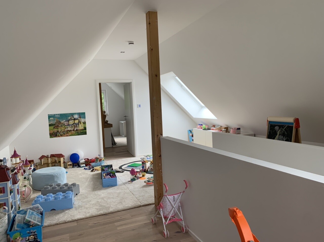 Dachgeschoss-Spielzimmer mit Holzbalken, Dachfenster, Spielzeug und Puppenwagen.