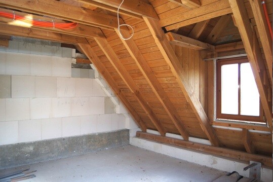 Dachboden mit sichtbaren Holzbalken, schräge Decke und Fenster, Bauarbeiten im Innenraum.