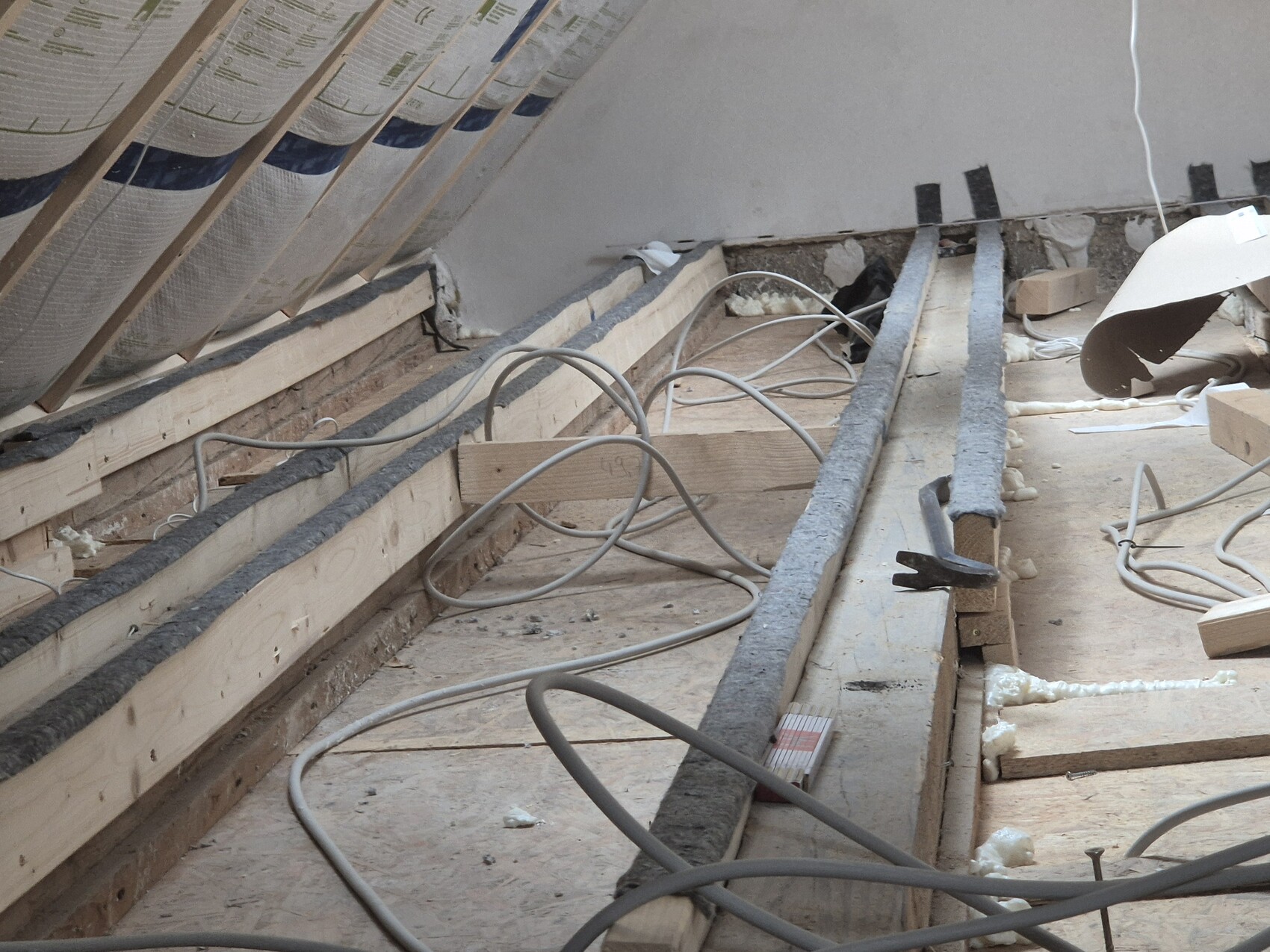 Offene Bauarbeiten im Dachgeschoss mit Kabeln, Dämmung und Baumaterialien.