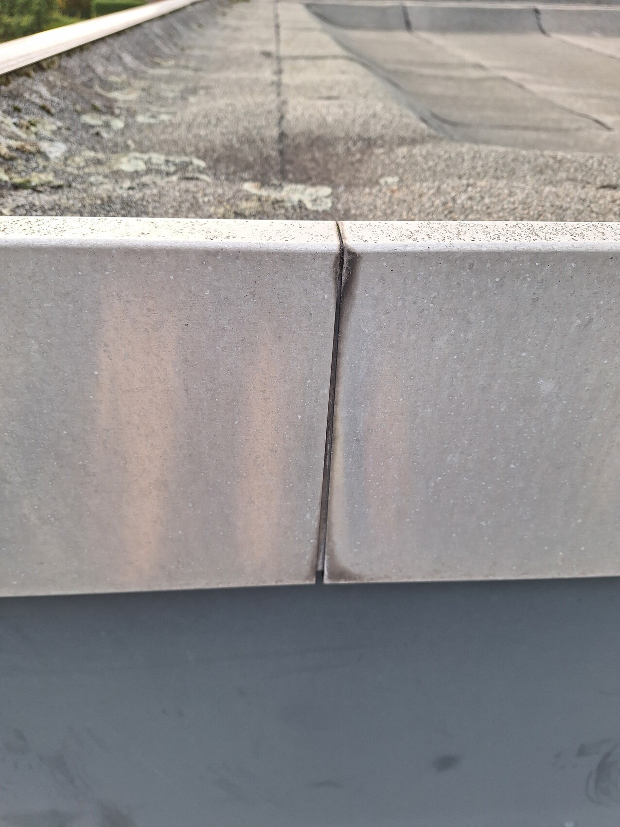 Nahaufnahme einer Dachkante aus Betonblöcken mit Fugen, Dachfläche mit Moosflecken.