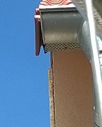 Nahaufnahme der Dachkante mit Ziegeln und Dachrinne vor blauem Himmel