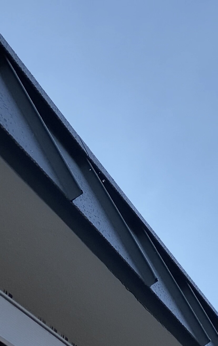 Draufsicht auf Dachkante und Regenrinne vor blauem Himmel.