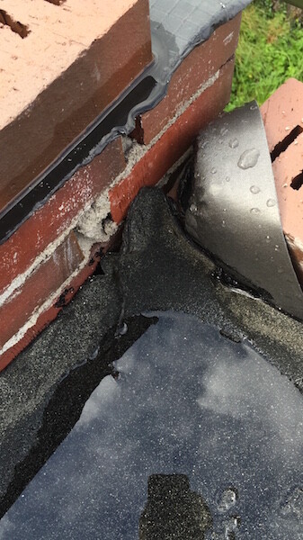 Nahaufnahme einer Dachkante mit brüchigem Mauerwerk, Dichtungsbelag und Wassertropfen
