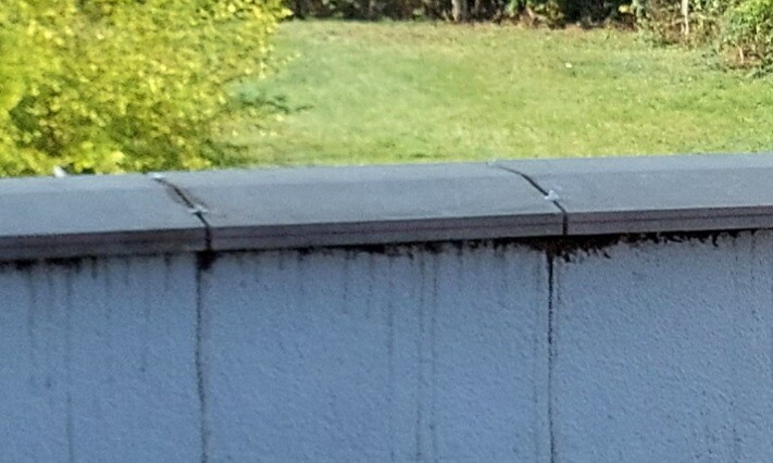 Flache Dachkante mit Blechabdeckung und Wasserflecken an weißer Wand