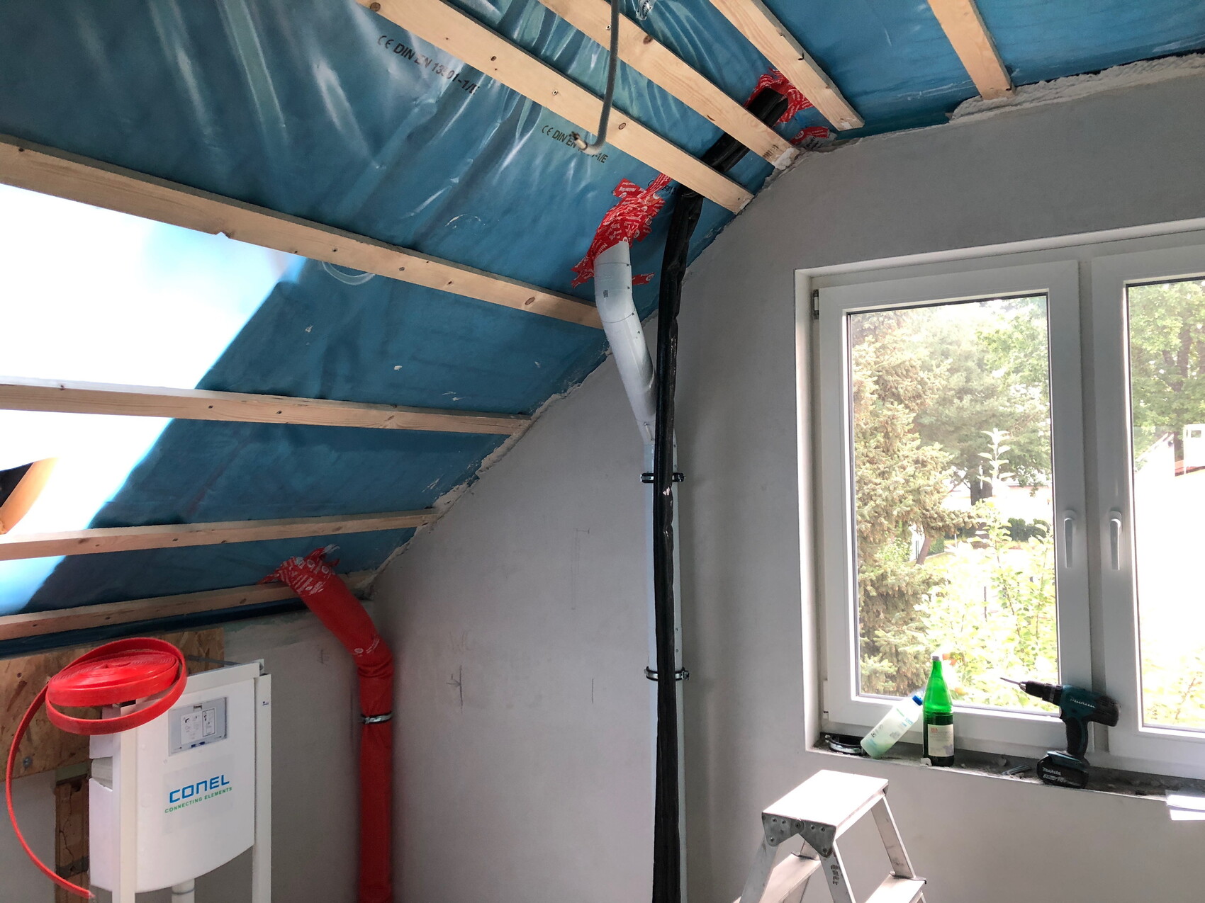Dachboden-Baustelle mit blauer Dämmung, Holzlatten, Rohren und einer Leiter.