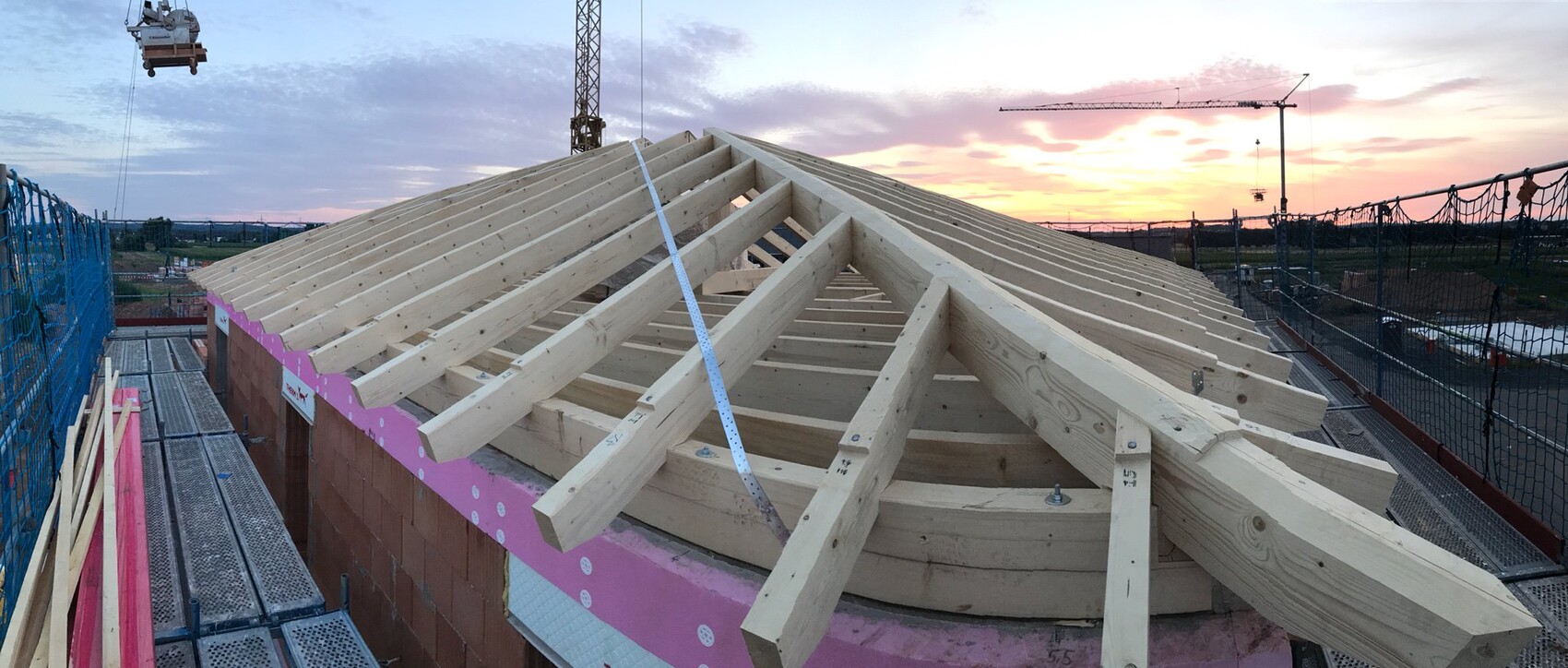 Holz-Dachkonstruktion auf Baustelle mit Gerüst bei Sonnenuntergang.