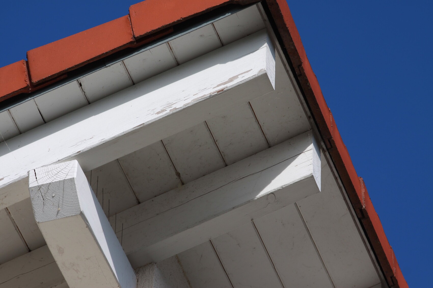 Nahaufnahme eines weißen Holzbalkens unter roten Dachziegeln gegen blauen Himmel