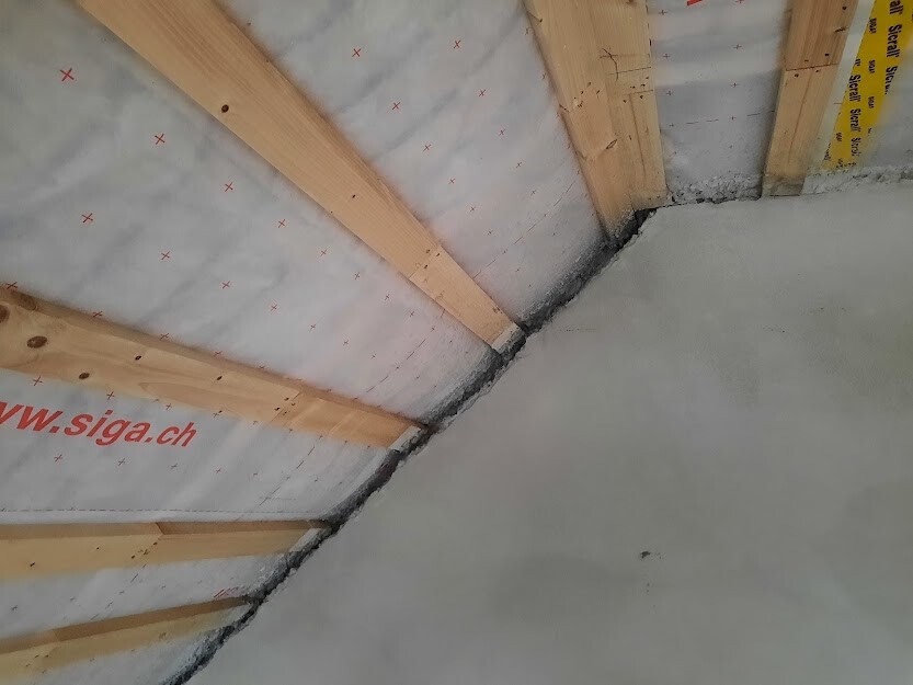 Unterkonstruktion eines Satteldaches: Holzbalken, Dämmstoffbahn, weiße Folie mit roten Kreuzen.