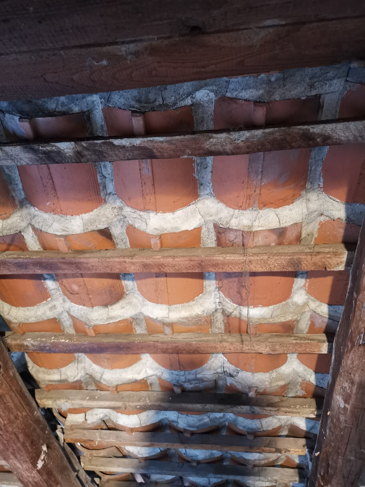Unterseite eines Daches: rote Tonziegel mit Mörtel zwischen Ziegeln und Holzbalken.